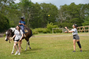Campers horseback riding with counselor guidance on an open field at Camp Lakota in Wurtsboro, New York