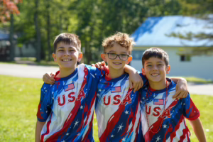 Three young boys wearing patriotic USA shirts smile together at Camp Lakota special event
